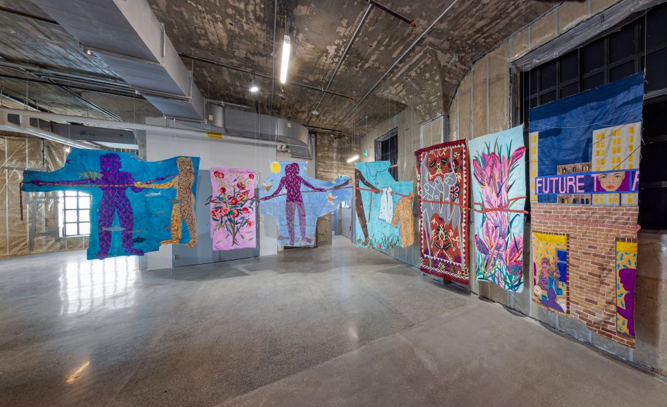 View of textile works hanging from the celing with human figures on them.