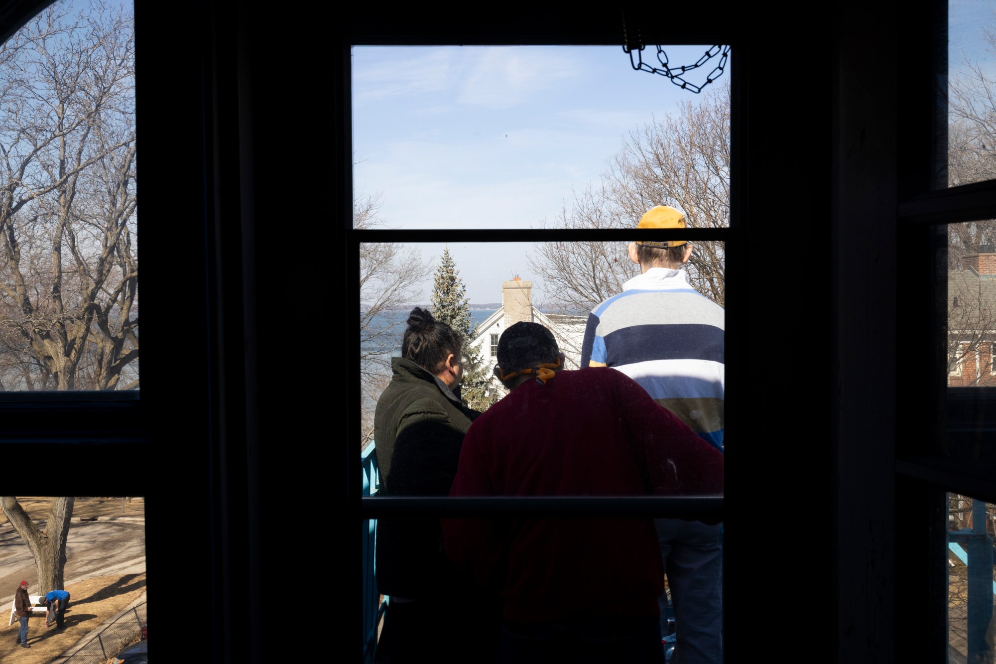 Three people stand outside a door, looking at the view of a lake and a house next to it.
